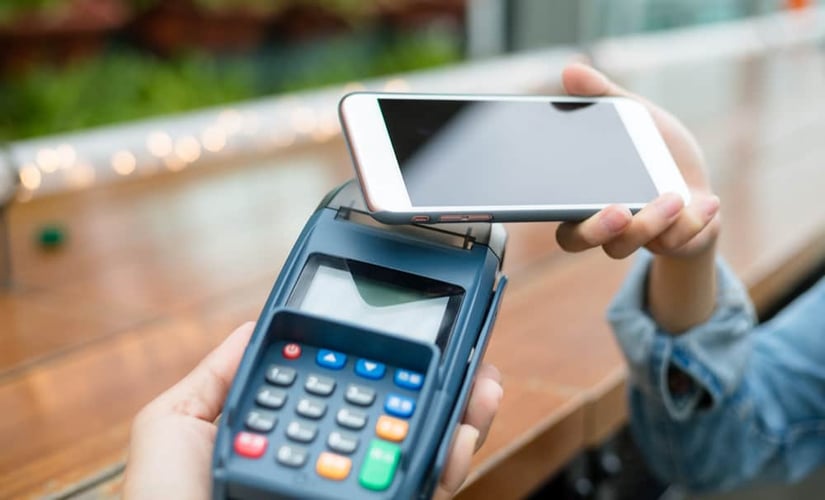 : a woman tapping her phone on a POS machine. Mobile payments are just one form of POS payments offered by POS lending startups