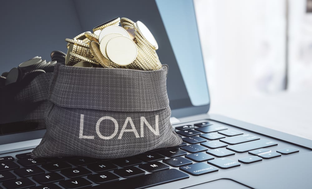 A bag of money sitting on a laptop implying an automated loan approval system.