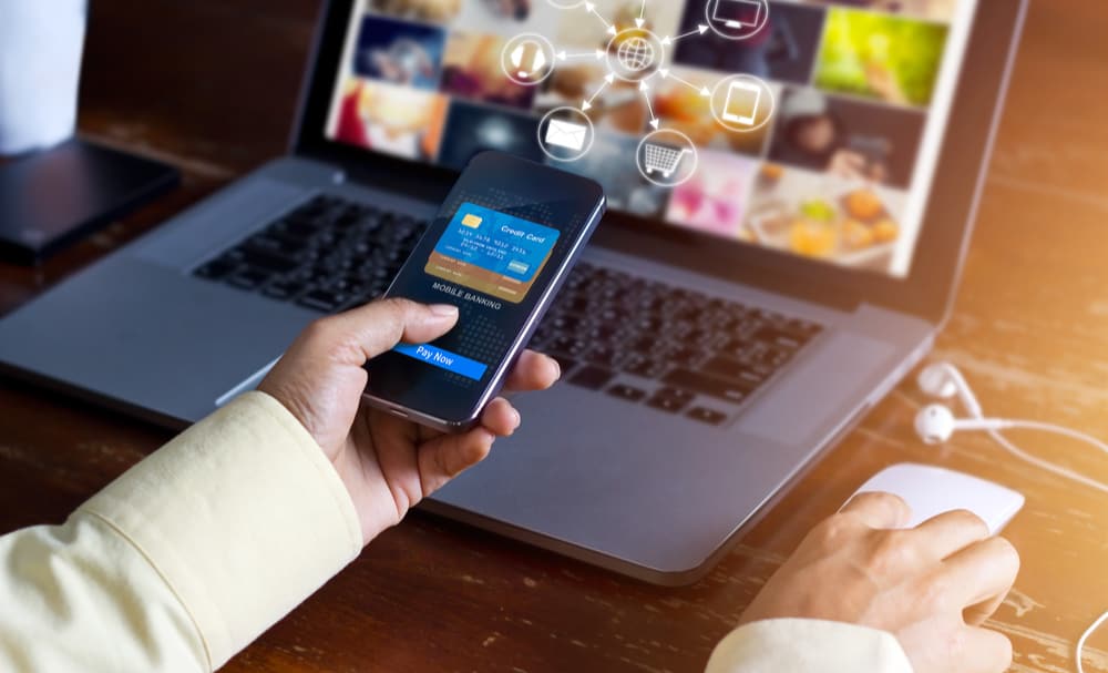  A person making a payment holding their phone and on a laptop representing omnichannel payment processing